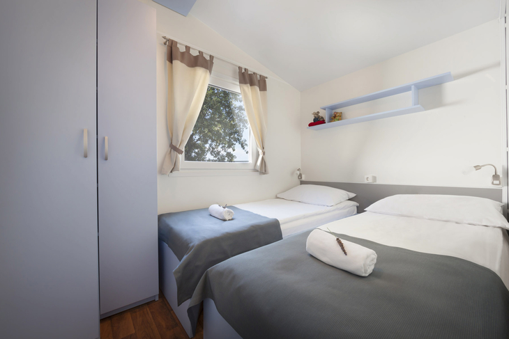 Zwei Einzelbetten in modernem Zimmer mit Vorhang und Schrank.