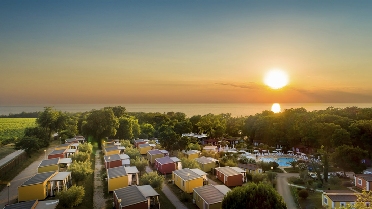 Luftaufnahme eines Campingplatzes mit Mobilheimen und Swimmingpool bei Sonnenuntergang.