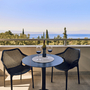 Balkon mit Tisch und zwei Stühlen, Blick aufs Meer und Landschaft im Hintergrund.