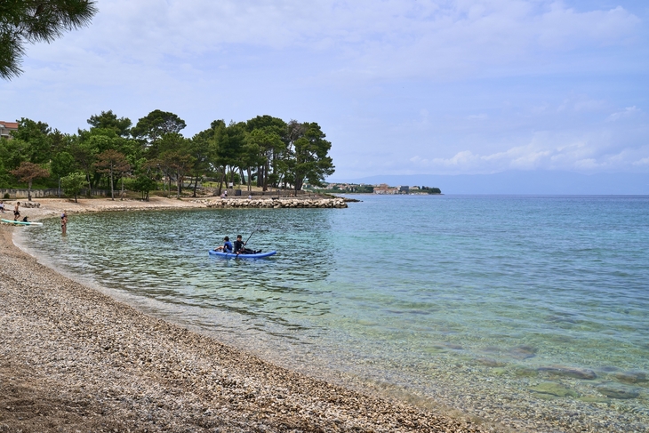 Strand bei Malinska, Krk mit klarem Wasser und Kajakfahrern.