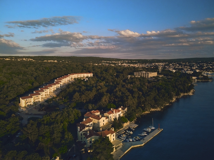 Küstenansicht von Malinska auf der Insel Krk mit Gebäuden und dichtem Wald am Meer.
