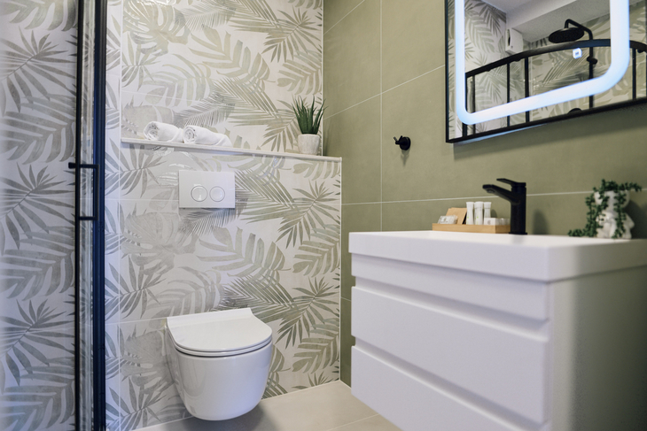 Modernes Badezimmer mit WC, Waschbecken und Spiegel, dekoriert mit Pflanzenmuster.
