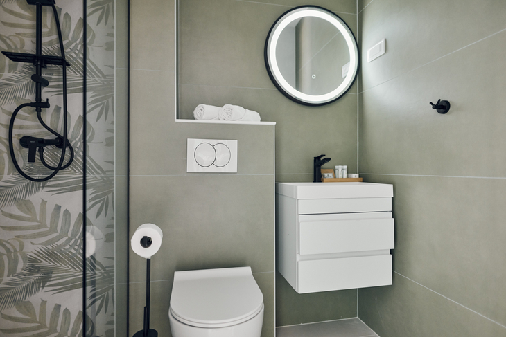 Modernes Badezimmer mit großer Dusche, rundem Spiegel und weißen Möbeln.
