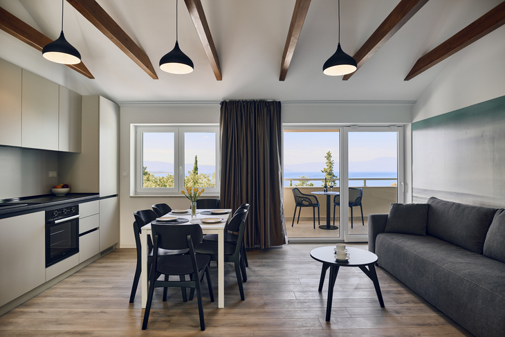 Wohnzimmer mit Sofa, Esstisch, Küche und Balkon mit Meerblick.