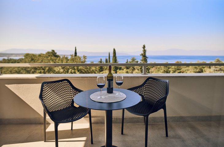 Balkon mit Tisch und zwei Stühlen, Blick aufs Meer und Landschaft im Hintergrund.