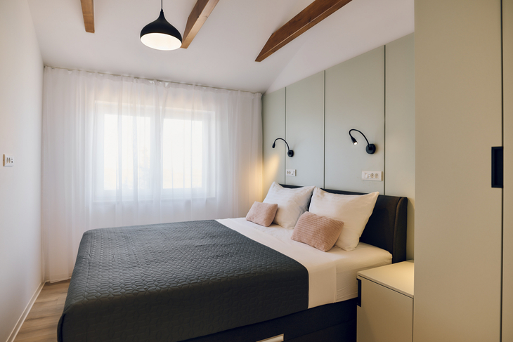 Schlafzimmer mit Doppelbett, Fenster, heller Vorhang und Nachttischen.