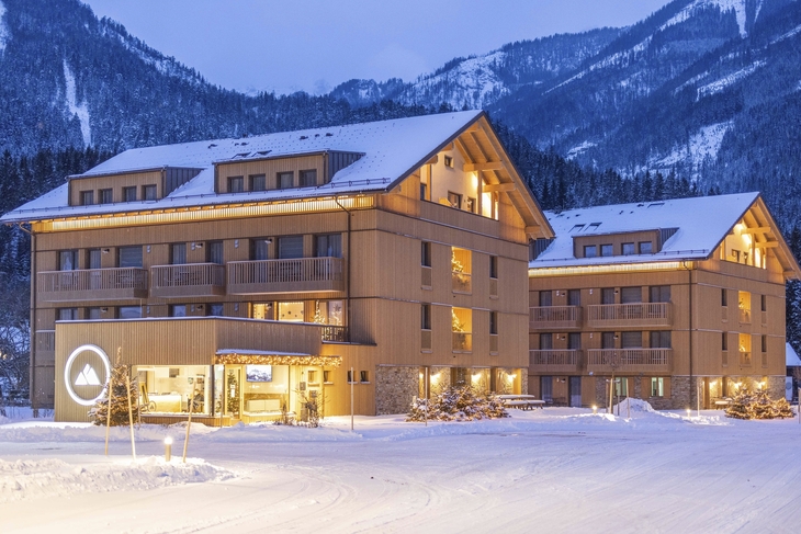 Verschneites Aparthotel in Berglandschaft bei Abenddämmerung.