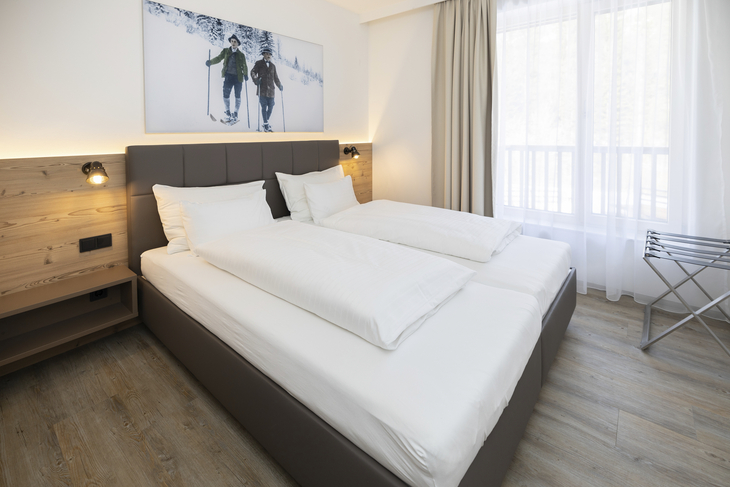 Helles Schlafzimmer mit Doppelbett, Holzwand und großem Fenster.