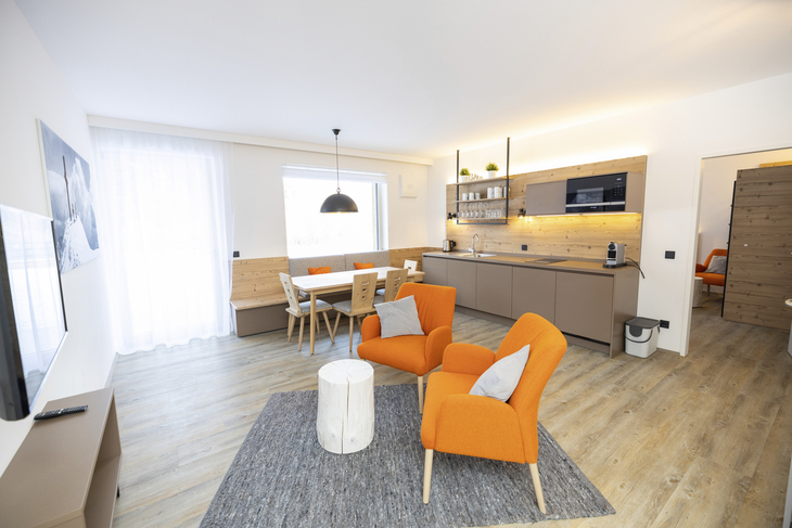 Wohnzimmer mit modernen Möbeln, Esstisch und offener Küche im Hintergrund.