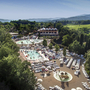 Luftaufnahme eines großen Ferienresorts mit Pools und Liegestühlen in grüner Umgebung.