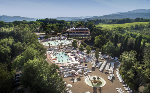 Luftaufnahme eines großen Ferienresorts mit Pools und Liegestühlen in grüner Umgebung.