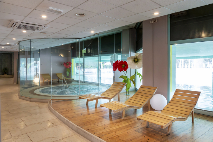 Wellnessbereich mit Liegestühlen und Whirlpool, umgeben von Glaswänden.