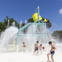Kinder spielen im Wasserpark mit Wasserspielgeräten und Spritzwasser.