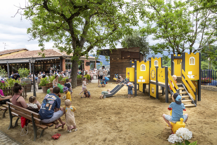 Kinder spielen auf einem Spielplatz mit Rutschen und Klettergerüsten im Grünen.