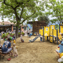 Kinder spielen auf einem Spielplatz mit Rutschen und Klettergerüsten im Grünen.