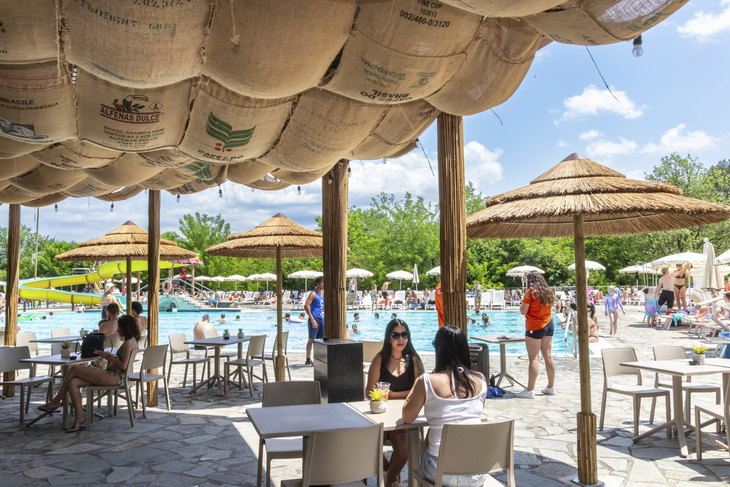 Terrasse am Pool mit Tischen und Strohschirmen im Norcenni Girasole Village, Toskana.