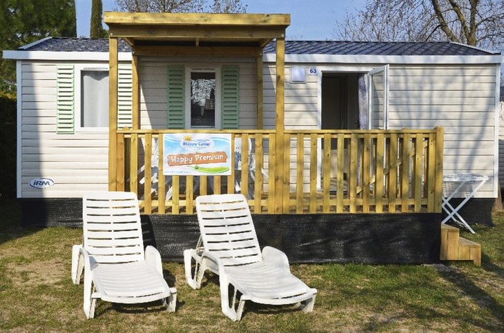 Mobilheim mit Veranda und zwei Sonnenliegen auf einer Wiese.