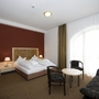 Hotelzimmer mit Doppelbett, Sofa, Tisch und Stühlen, Blick auf großes Fenster.