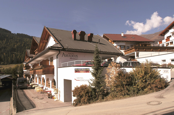 Gebäudeansicht des Hotels Amadeus Micheluzzi in Serfaus mit umliegender Landschaft.