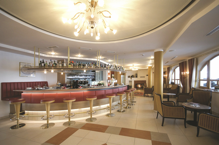 Moderne Hotellobby mit Bar, roten Hockern und gemütlichen Sitzbereichen.