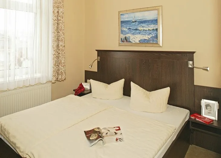 Helles Schlafzimmer mit Doppelbett, Kunst an der Wand und einem offenen Magazin auf dem Bett.
