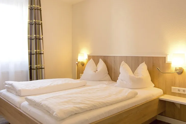 Helles Schlafzimmer in einer Ferienanlage mit Doppelbett und Nachttischlampen.