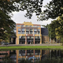 Ansicht des Amrath Hotels Alkmaar mit Bäumen und Wasser im Vordergrund.