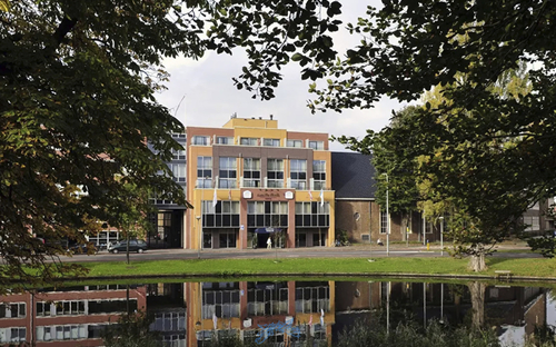 Ansicht des Amrath Hotels Alkmaar mit Bäumen und Wasser im Vordergrund.