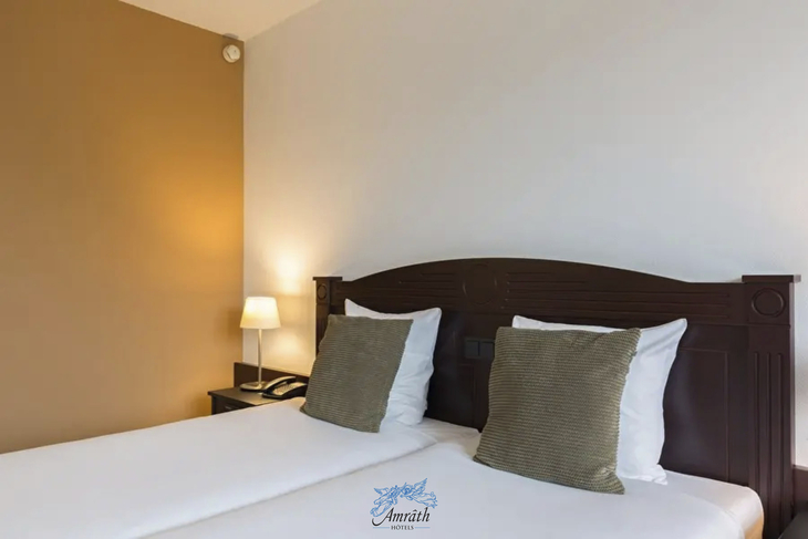 Hotelzimmer mit zwei Einzelbetten, Nachttisch und Lampe im Amrâth Hotel Alkmaar.