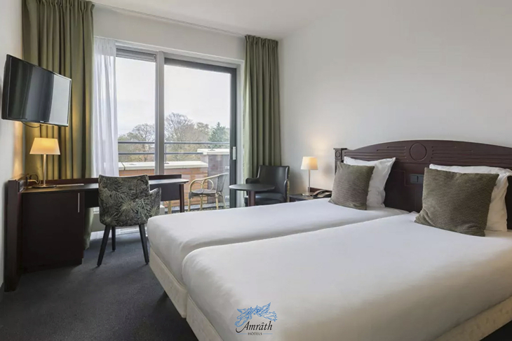 Hotelzimmer mit zwei Einzelbetten, Schreibtisch, Stuhl und TV.