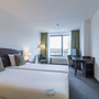 Hotelzimmer mit zwei Betten, Schreibtisch, Lampe und Fenster mit Vorhängen.