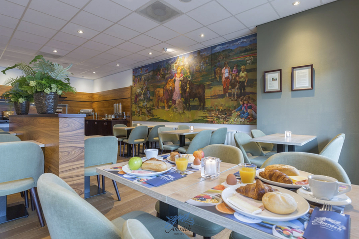 Hotelrestaurant mit gedecktem Frühstückstisch und Wandbild im Hintergrund.