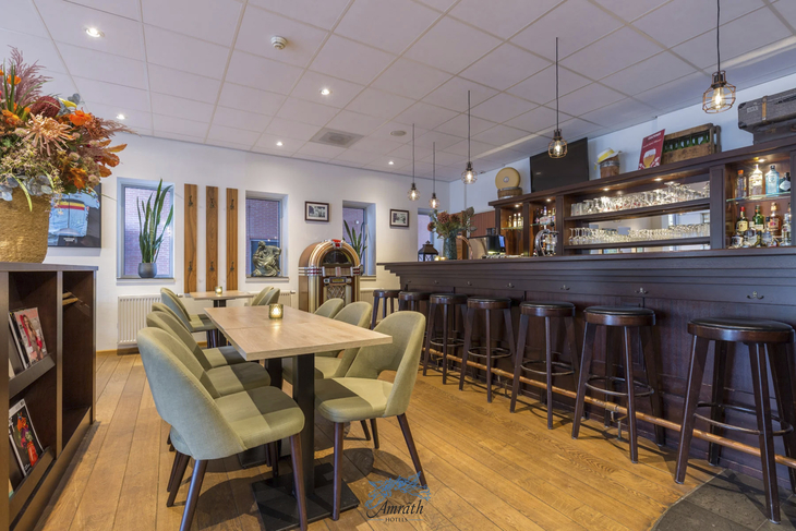 Innenraum einer Hotelbar mit Holztresen und grünen Stühlen.