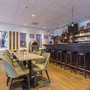 Innenraum einer Hotelbar mit Holztresen und grünen Stühlen.