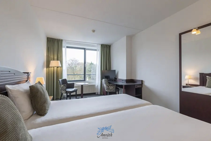 Helles Hotelzimmer mit zwei Einzelbetten, Schreibtisch und großem Fenster.