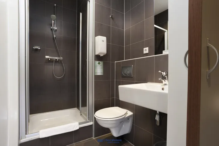 Badezimmer mit Dusche, WC und Waschbecken in dunklen Fliesen gehalten.
