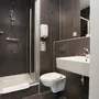 Badezimmer mit Dusche, WC und Waschbecken in dunklen Fliesen gehalten.