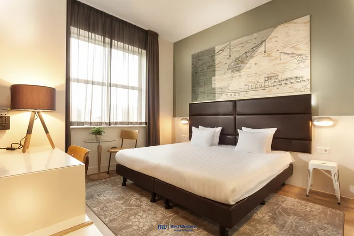 Hotelzimmer mit Doppelbett, Lampe, großem Fenster und Wandkunst in modernem Stil.