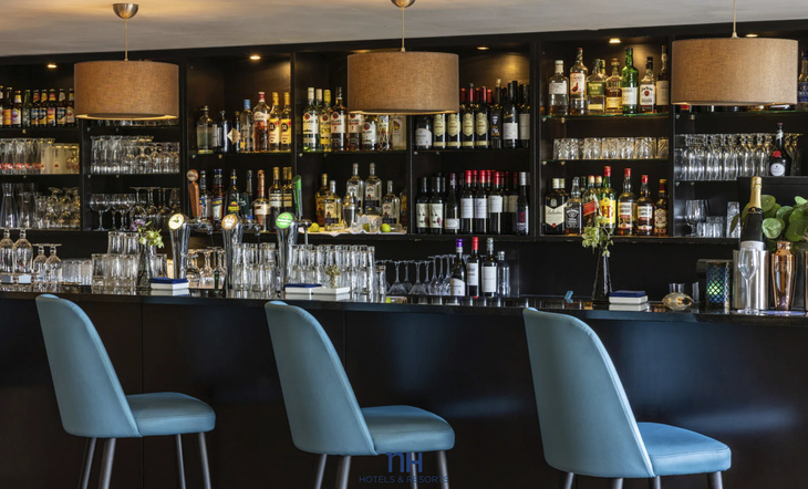 Hotelbar mit blauen Stühlen und Regalen voller Flaschen und Gläser.