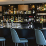 Hotelbar mit blauen Stühlen und Regalen voller Flaschen und Gläser.