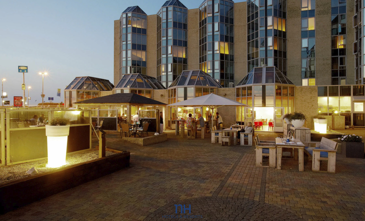 Terrasse des NH Hotels Zandvoort bei Abenddämmerung mit Sitzbereichen und Beleuchtung.