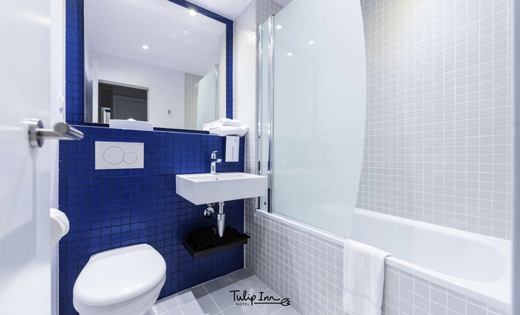 Badezimmer im Hotel Tulip Inn, modern eingerichtet mit WC, Waschbecken und Badewanne.