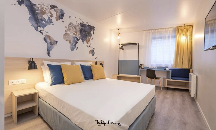 Hotelzimmer mit Doppelbett, Weltkarten-Wanddeko und Schreibtisch in Antwerpen.