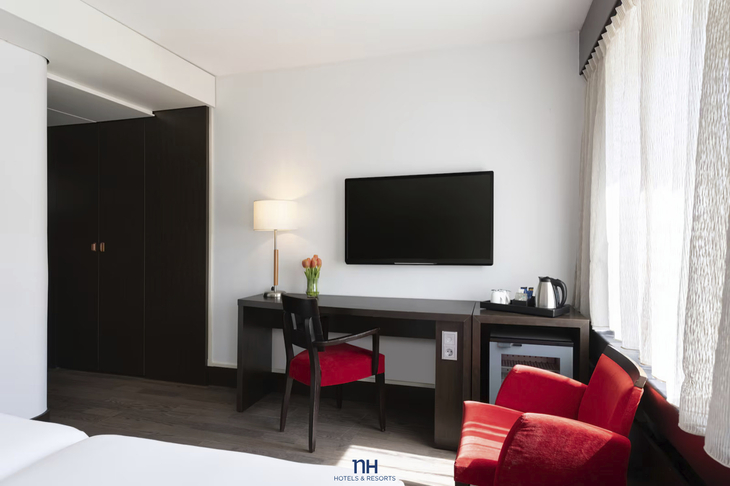 Hotelzimmer mit Schreibtisch, Stuhl, Fernseher und rotem Sessel.