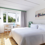 Helles Hotelzimmer mit Doppelbett, Tisch und großem Fenster mit Blick ins Grüne.