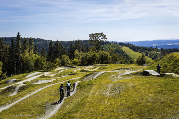 Radfahrer auf einem kurvigen Bikepark mit Wald und Hügeln im Hintergrund
