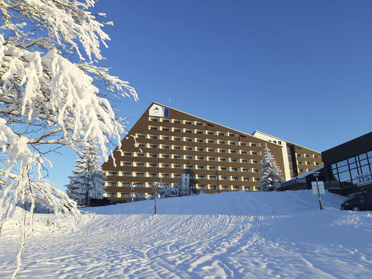 Schnee bedeckter Hotel- und Ferienpark in winterlicher Landschaft unter blauem Himmel.