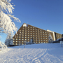 Schnee bedeckter Hotel- und Ferienpark in winterlicher Landschaft unter blauem Himmel.