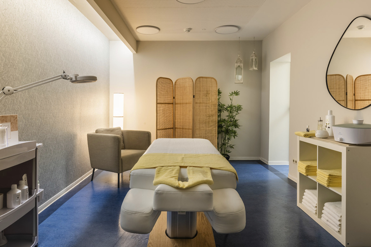 Massageraum mit Liege, Stühlen und Entspannungsdekoration.
