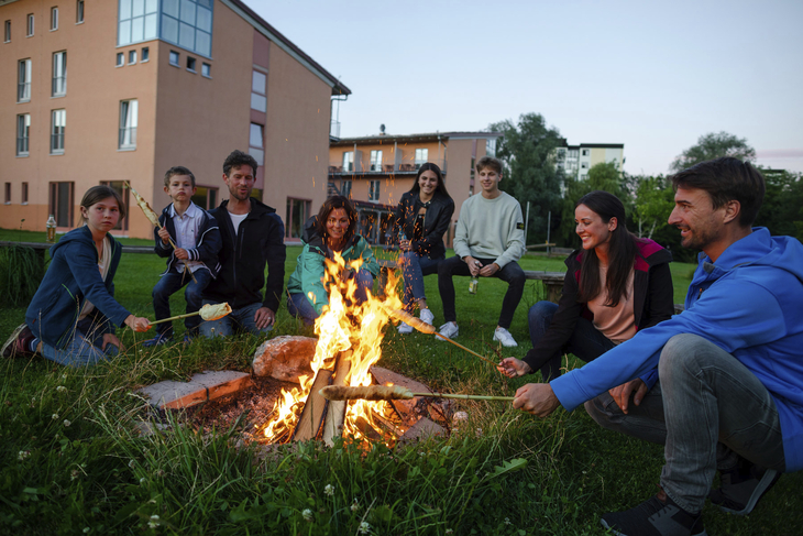 Gruppe von Menschen sitzt um ein Lagerfeuer vor einem Hotelgebäude.